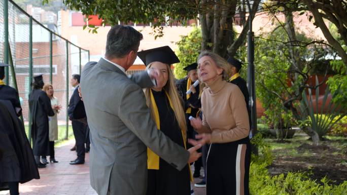 自豪的父母在毕业典礼后与女儿交谈，拥抱并微笑