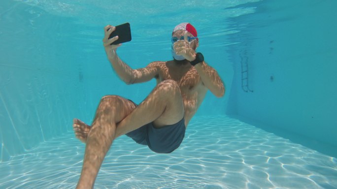 夏季游泳池中戴防冠状病毒面罩的男子水下自拍