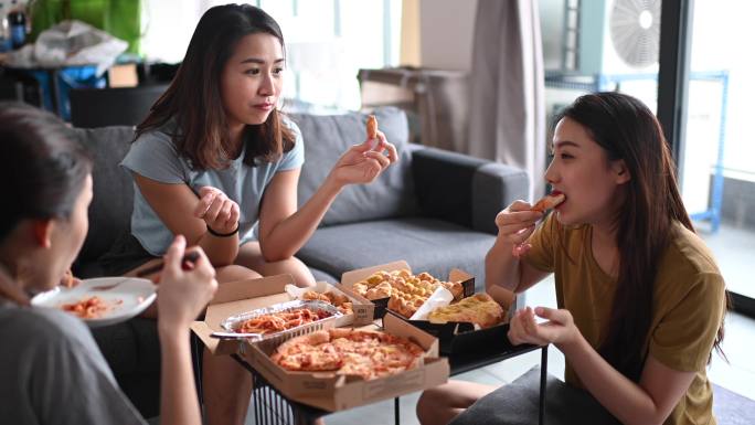 3位亚裔中国女性朋友在起居室吃比萨饼作为午餐