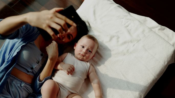 妈妈和她的孩子睡觉了。用手机在床上互相拍照。它代表着母婴之间的爱和温暖。谁想一起拍一张令人印象深刻的