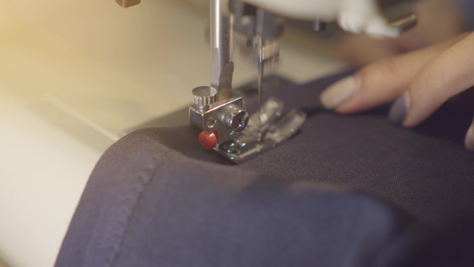 女性手拿牛仔布在缝纫机上，特写。服装维修、回收、家庭爱好和在家工作的概念。