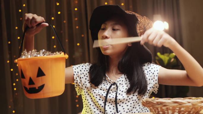 在家里的晚上，一个戴着巫师帽、手持魔杖的亚洲女孩在万圣节的概念游戏中玩耍。