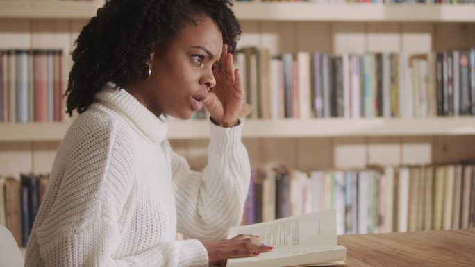 一位非洲裔女性在客厅里读着迷人的书。情节扭曲的情绪反应。