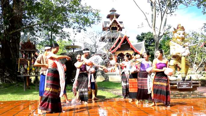 慢动作泼水节-美丽的男女穿着泰国传统服装，在寺庙背景上与大象一起泼水