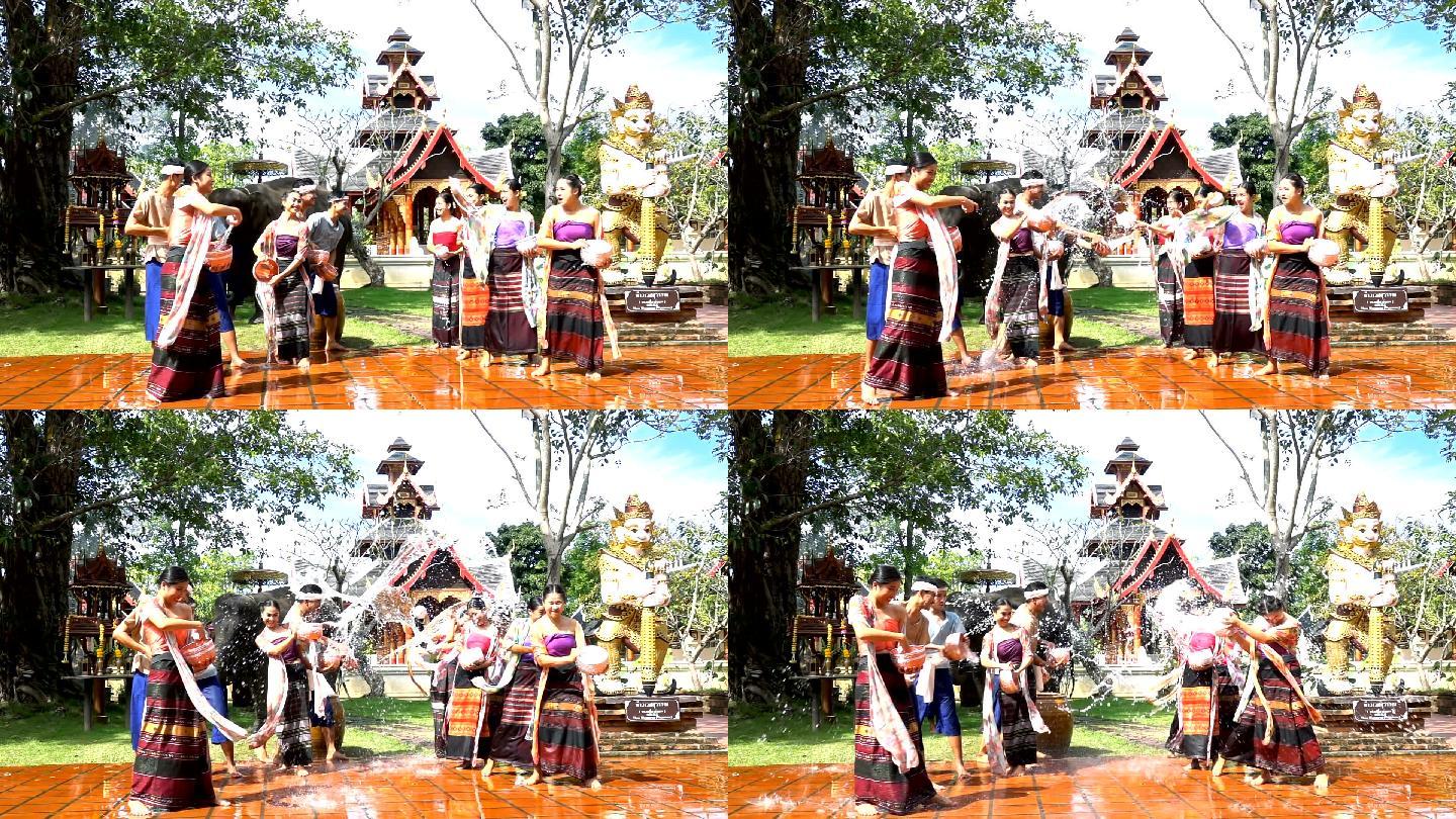 慢动作泼水节-美丽的男女穿着泰国传统服装，在寺庙背景上与大象一起泼水