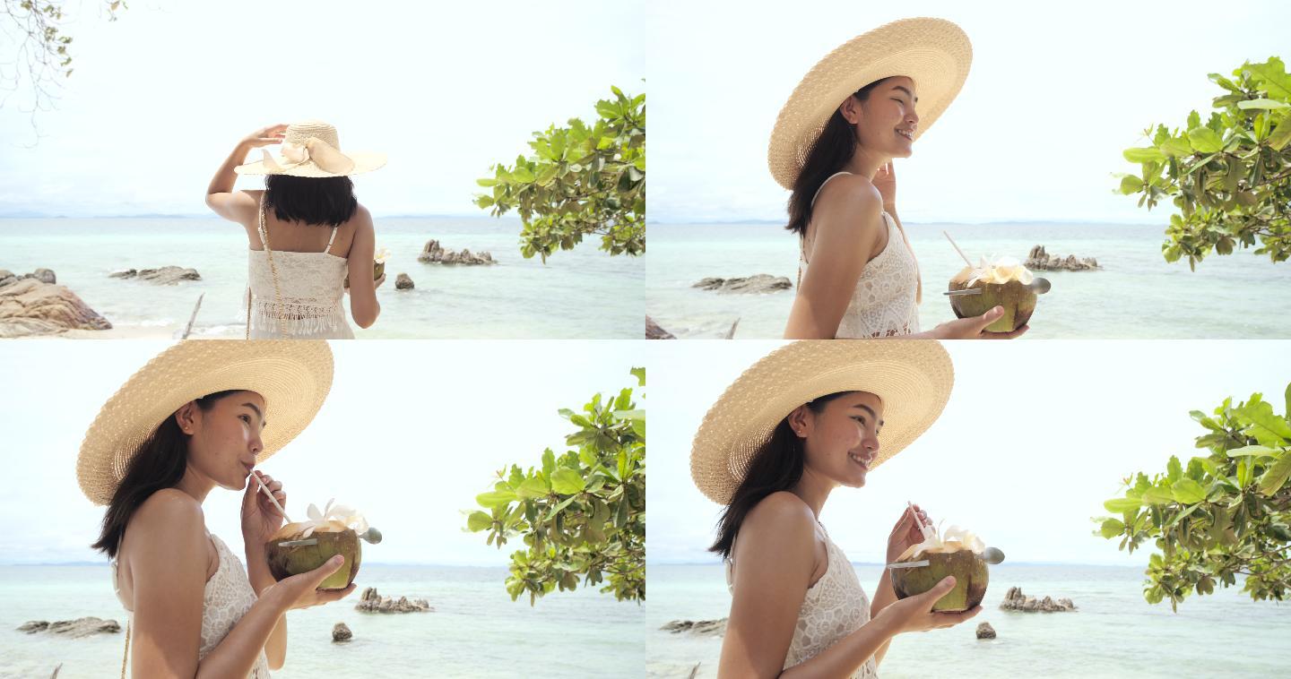 美丽的亚洲年轻女子在海滩上喝着椰子水。
