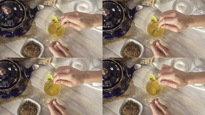 一张白色乡村桌子上，一位女士双手向热茶甘菊输液杯中倒入和搅拌一茶匙糖的高角度特写照片