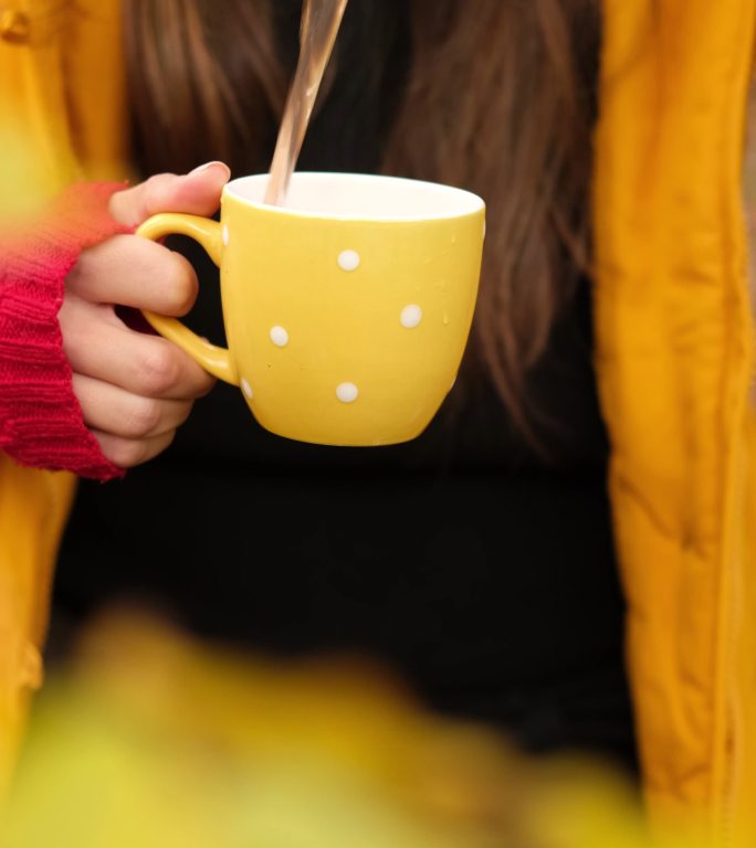 森林里，一个穿着黄色派克大衣的女人从保温瓶里倒茶。