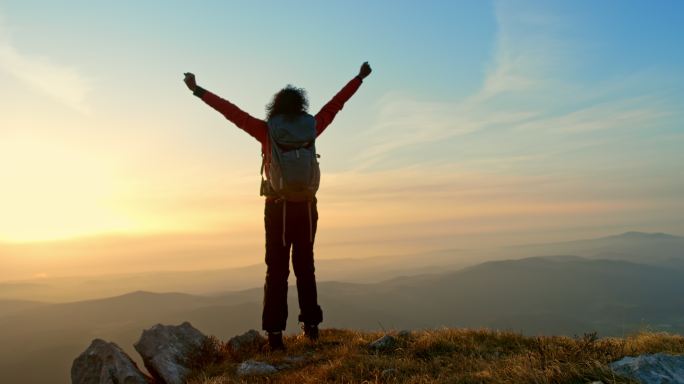 落日时分，一位名叫斯洛·莫的女性徒步旅行者站在山顶上，双手高举