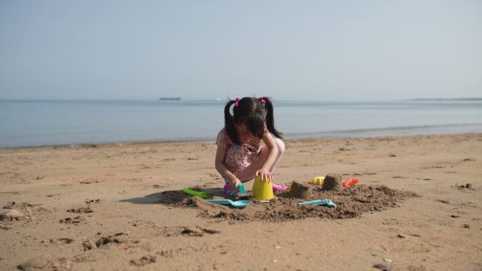 年轻女孩在夏日海滩上建造金沙城堡