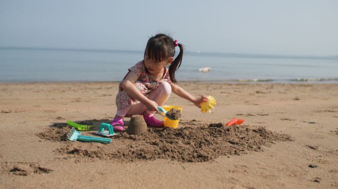 年轻女孩在夏日海滩上建造金沙城堡
