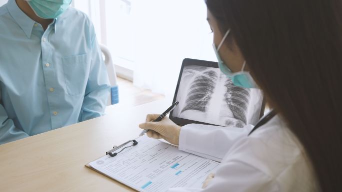 专业医生戴上口罩解释病人，并在笔记本电脑屏幕上显示肺部x光图像。医生穿着长袍在诊所病房与疑似感染冠状