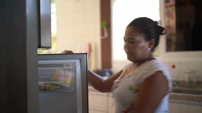 成熟的女人在家里从冰箱里拿起沙拉碗