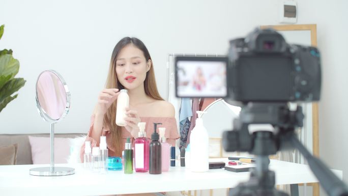 这位美丽的亚洲女性博主正在展示如何化妆和使用化妆品。在摄像机前录制家中的vlog视频直播。商业在线对