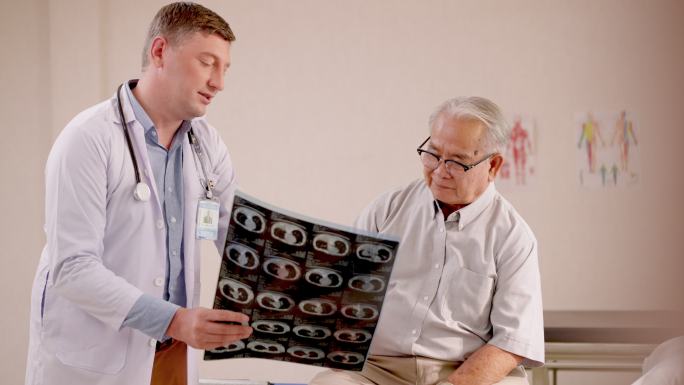 专业男医生照片，显示并诊断老年男性患者腹部的x射线扫描结果。放射科医生在医院病房与患者一起查看x射线