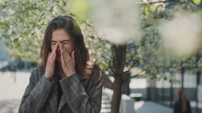 春季过敏。站在城市街道上头痛的女人