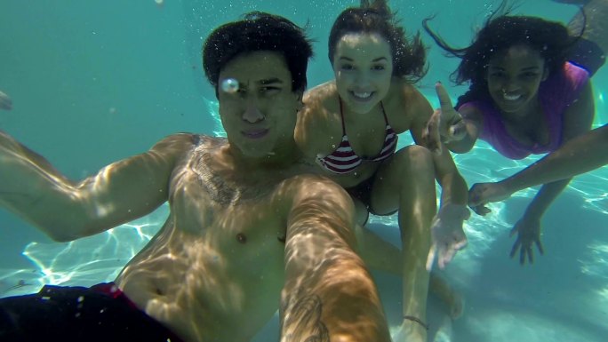 游泳池里不同的青少年在水下对着摄像机微笑