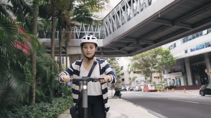 周末，亚裔中国女游客在城市里骑着电动推式踏板车微笑着看着远方