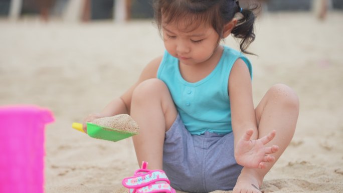 亚洲可爱的蹒跚学步的小女孩白天坐在沙滩上玩沙堡。