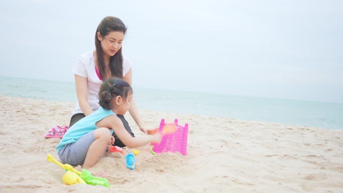 暑假期间，女儿和母亲在沙滩上玩沙堡。
