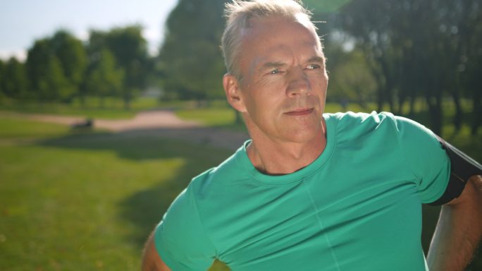 一个阳光明媚的夏日早晨，一位身穿绿松石t恤的斯堪的纳维亚健身教练正在公园里热身