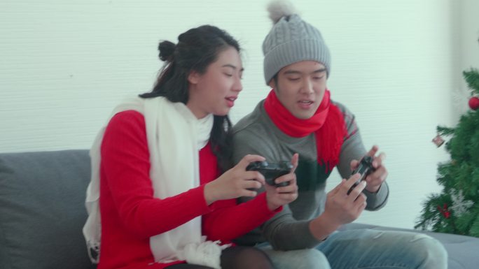 亚洲年轻夫妇在家一起玩游戏，按下游戏手柄按钮