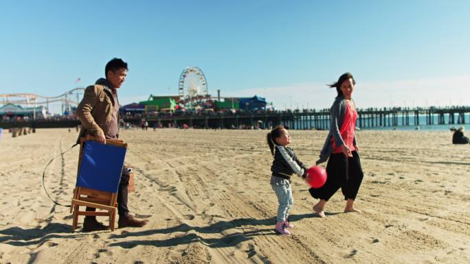 一家人走过圣莫尼卡海滩时，小女孩在扔球