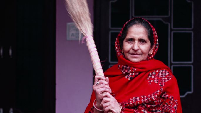 一名印度妇女手持扫帚对着镜头微笑