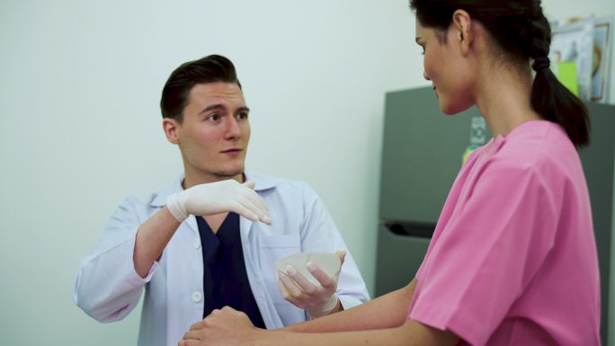 男整形外科医生向患者展示硅胶乳房植入物。