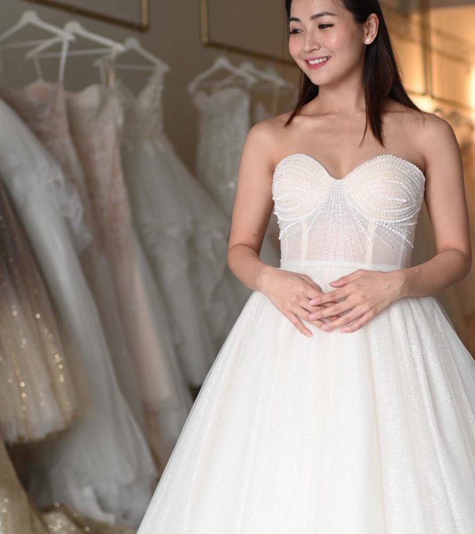快乐自豪满意的亚洲华人新娘肖像摆姿势看着相机在婚纱店微笑着试穿婚纱