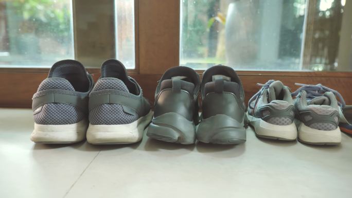 场景中父亲的鞋子和母亲的鞋子紧挨着儿子的鞋子，在家门口附近，家庭物品的概念