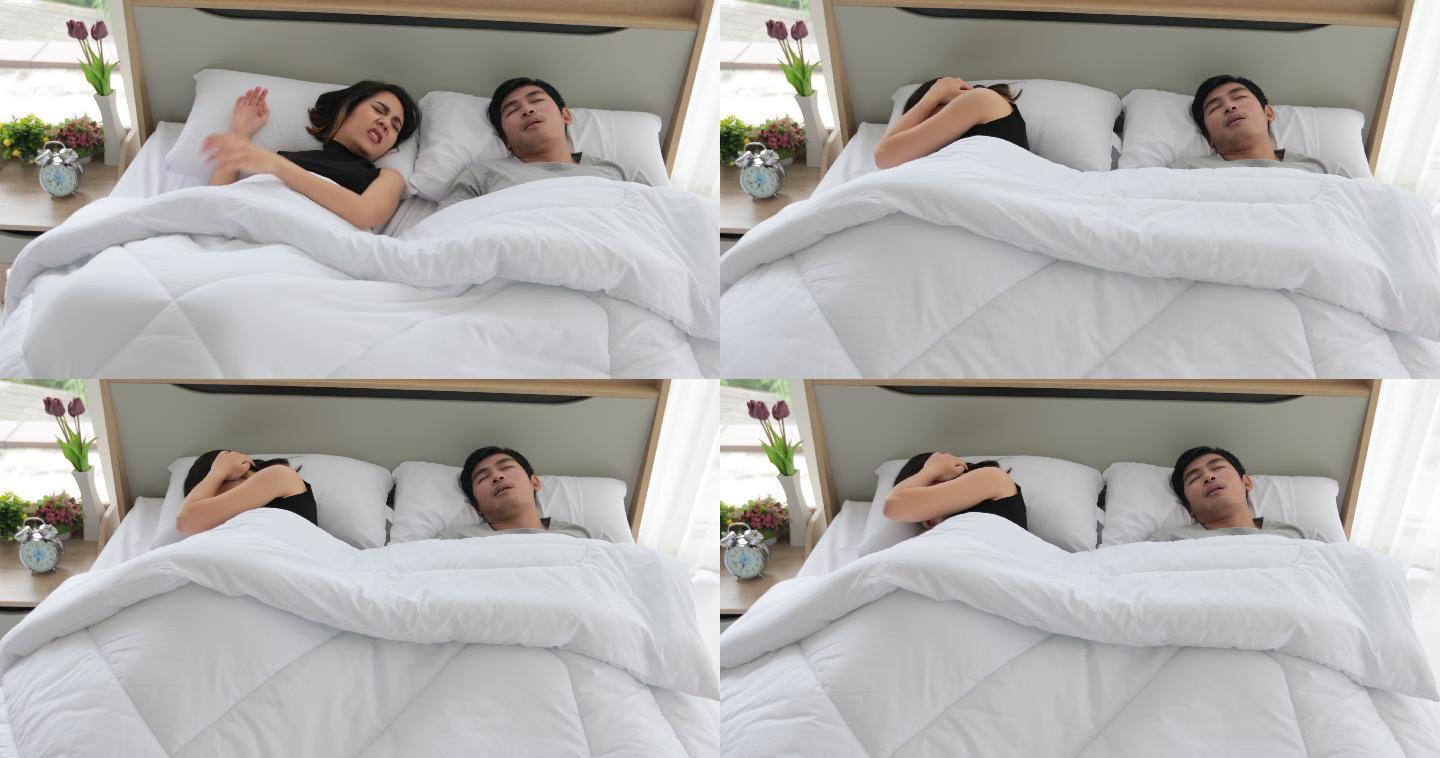 亚洲年轻的妻子睡不着，丈夫在她身边打鼾，女人用枕头捂住耳朵。