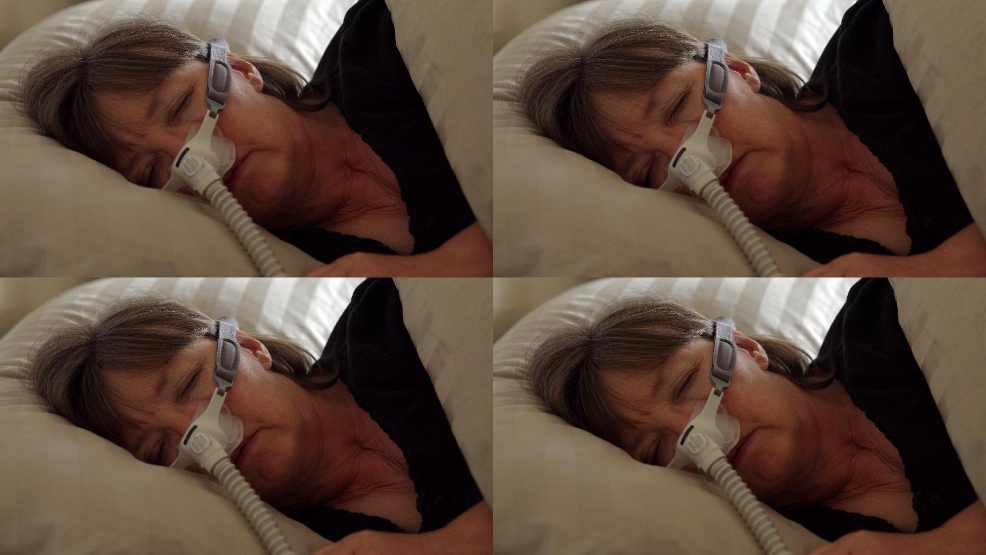 患有睡眠呼吸暂停症的中年女性在床上睡觉时，戴着CPAP（持续气道正压通气）机器帮助睡眠
