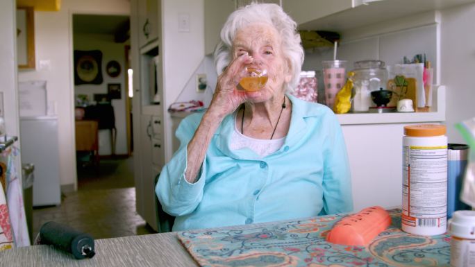 老年妇女饮用橙色混合饮料作为日常维生素补充剂或药物