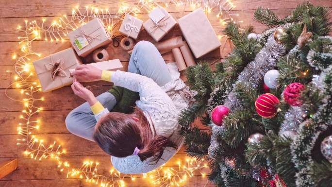 2019冠状病毒疾病流行期间，一名妇女在圣诞树下用回收材料包装礼物，准备圣诞节假期。新常态。