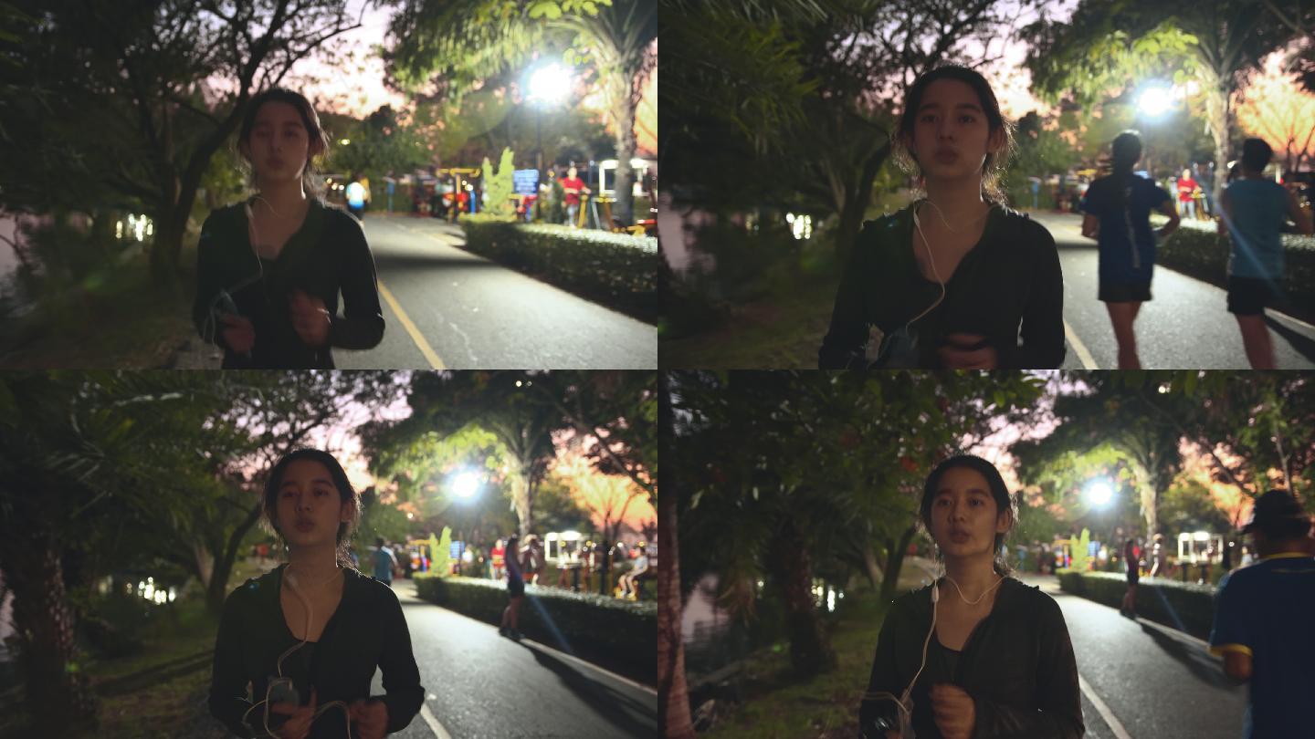 迷人的亚洲少女一边在公园跑步一边听音乐。年轻女子在夜间慢跑锻炼。