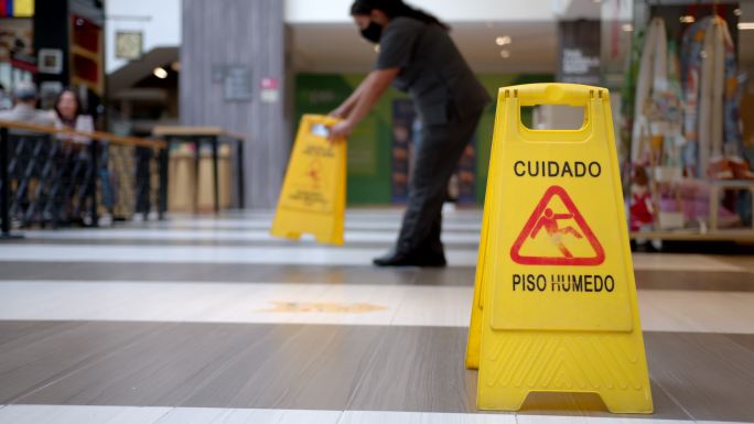 商场女清洁工在地板干燥时张贴湿滑警告标志
