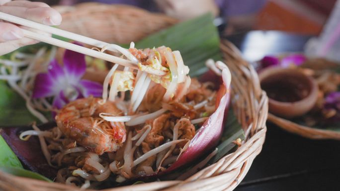 在盘子上用筷子吃虾垫泰式面条，在一张古老的绿松石木板桌上放香蕉叶，面条是用新鲜的水蒸汽加热制成的