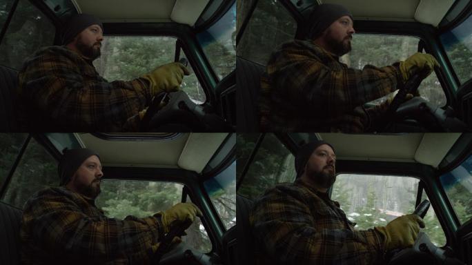 一位30多岁留着胡子的白种人在一个雪天的常绿森林里开着卡车