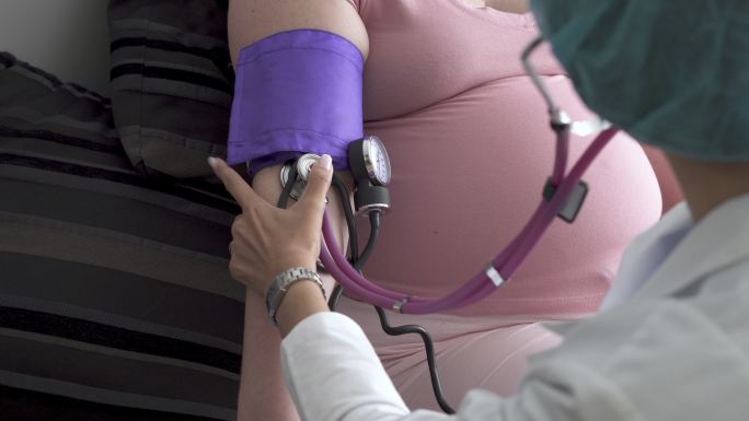 孕妇在家由医生给她看病，医生给她量血压