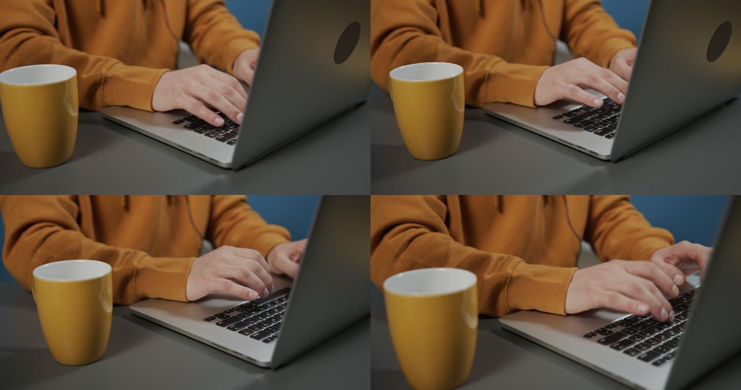 一只穿着黄色连帽衫的男性手在笔记本电脑上输入文本的高角度视图
