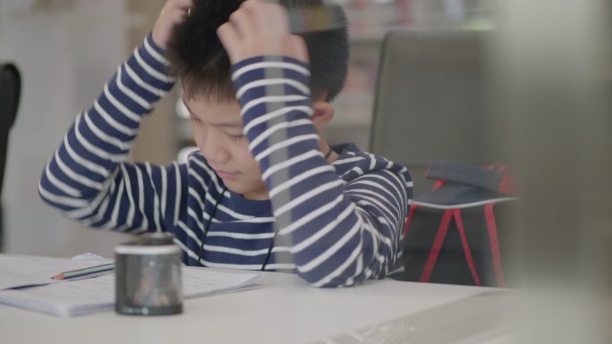 亚洲小男孩坐在图书馆做作业，茫然无聊，不想工作