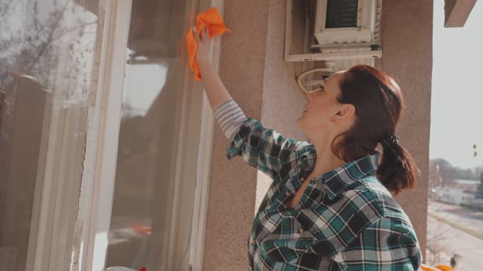 女士，用抹布和喷雾瓶中的清洁产品清洁并擦拭阳台窗户