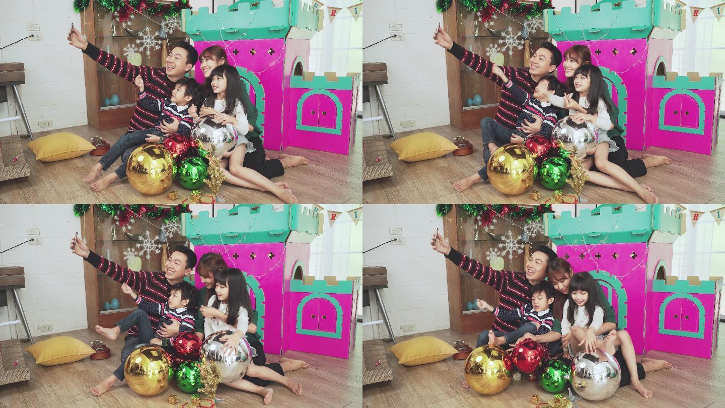 一个亚洲家庭坐在地板上和纸做的家庭玩具一起准备圣诞节。12月的假期，父亲用智能手机拍摄集体自拍照片，