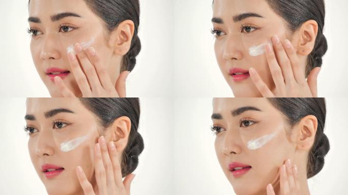 亚洲女性在白色背景上涂抹护肤面霜。美丽的女人用幸福的情感抚摸着她的脸。富有表情的面部表情。美容和水疗