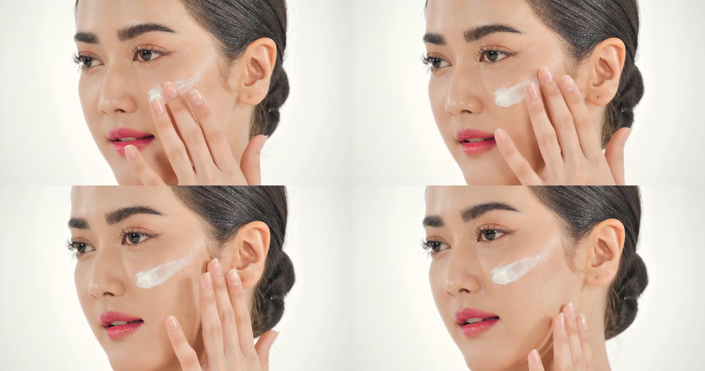亚洲女性在白色背景上涂抹护肤面霜。美丽的女人用幸福的情感抚摸着她的脸。富有表情的面部表情。美容和水疗