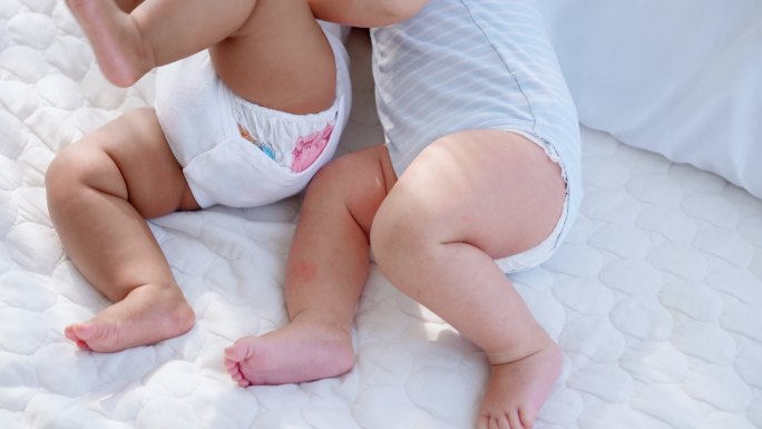 两个可爱的黑白相间的新生儿躺在白色卧室里，双腿的特写镜头正在玩耍，并愉快地交叉着交错的双腿。