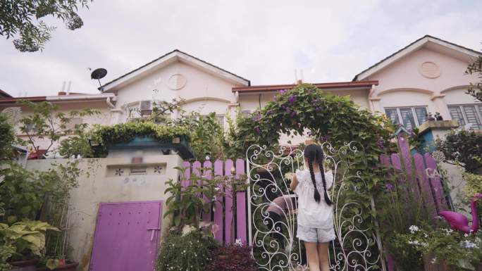 在晨曦中，欢快的亚裔中国小女孩关上了挂满牵牛花的房子院子的门
