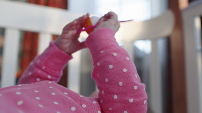 可爱快乐的女婴，穿着粉色连体衣，戴着玩具拨浪鼓，在阳光明媚的早晨在室内玩得很开心