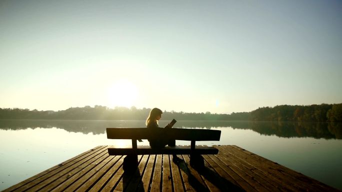 年轻女子在湖边的长凳上看书